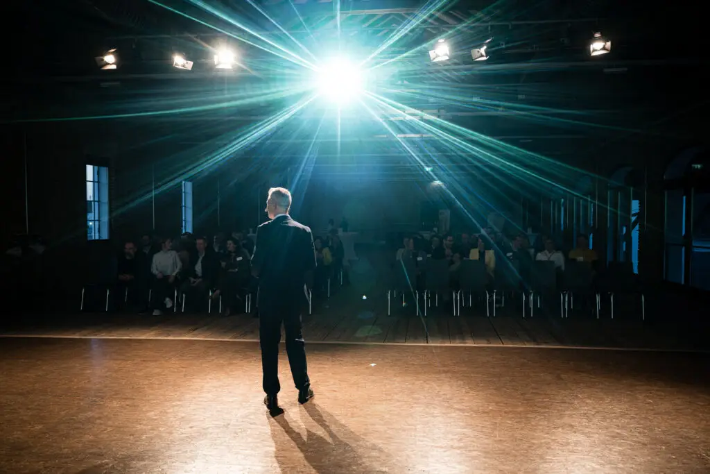 Eventfotografie eines Business-Vortrags vor Publikum mit starkem Bühnenlicht